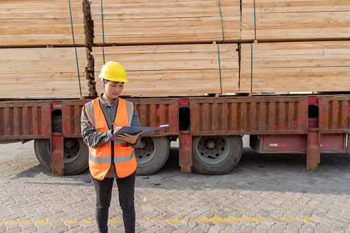 The female worker next to the truck is checking the wood data