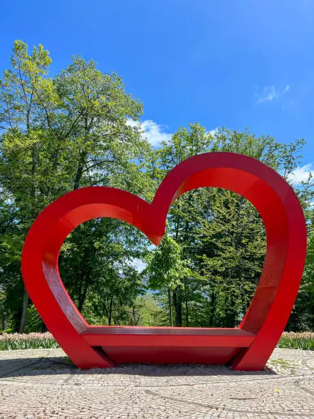 Photo of big red heart over green trees and beautiful blue sky in a sunny day at a park