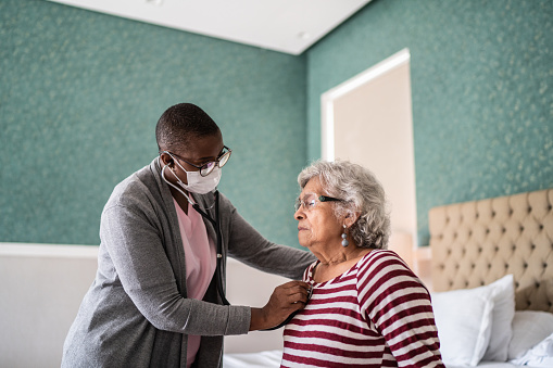 Doctor examing a senior woman in the bedroom - wearing a face mask