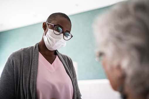 Nurse talking to senior patient's woman - using protective face mask