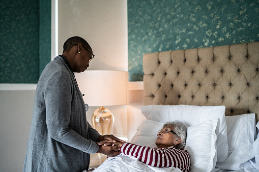 Nurse helping a senior woman lying down in the bed