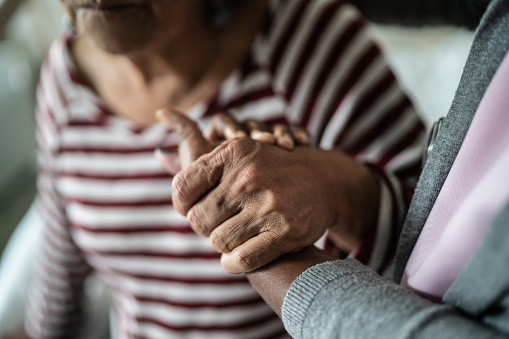 Nurse or home caregiver and senior woman holding hands at home