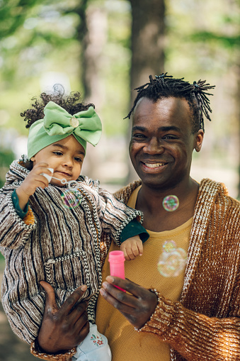 African american father spending time with his daughter in the park. Father's day. Father's love. Portrait of a baby girl and her father blowing soap bubbles.