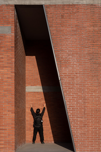 An Asian woman raises her hand in a red brick house