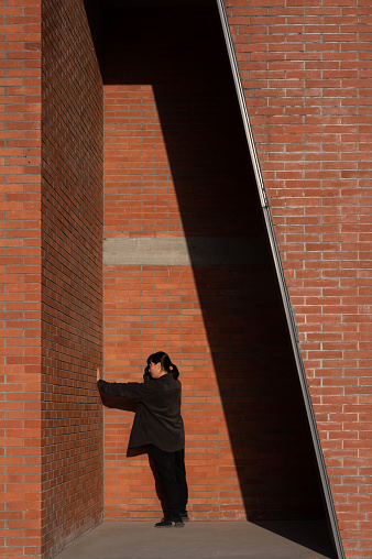An Asian woman pushes a wall in a red brick house with sunshine