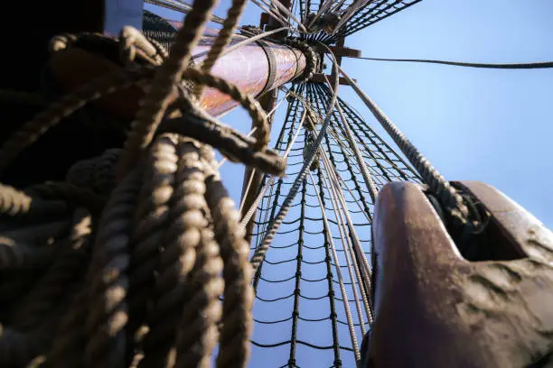 Photo of Mast and rigging of old wooden VOC sailing ship with ropes, rope loaders and pulleys