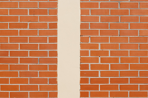 Close-up on a brick wall divided by a cream colored pillar.