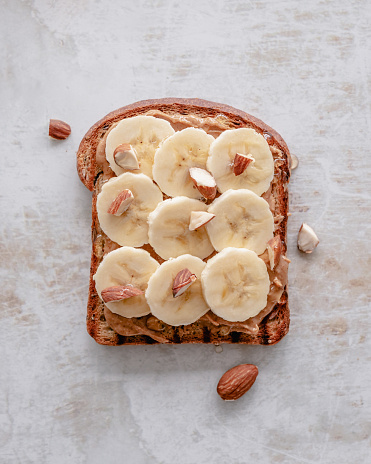 Overhead view of a toasted bread slice topped with peanut butter, banana slices, chopped almonds and a drizzle of honey