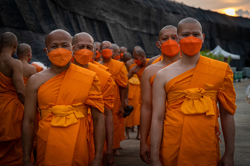 Two young Asian monk stay with other monk on green big buddha statue to clean in area of body of statue with warm light of early morning.