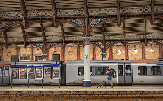York, UK. April 27, 2022.  Railway carriages under a historic canopy. A notice board with advertisements is beside a column and a woman and dog are on he platform.