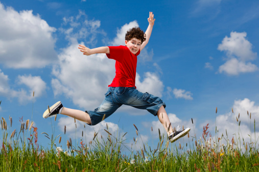 Boy running, jumping outdoor against blue sky