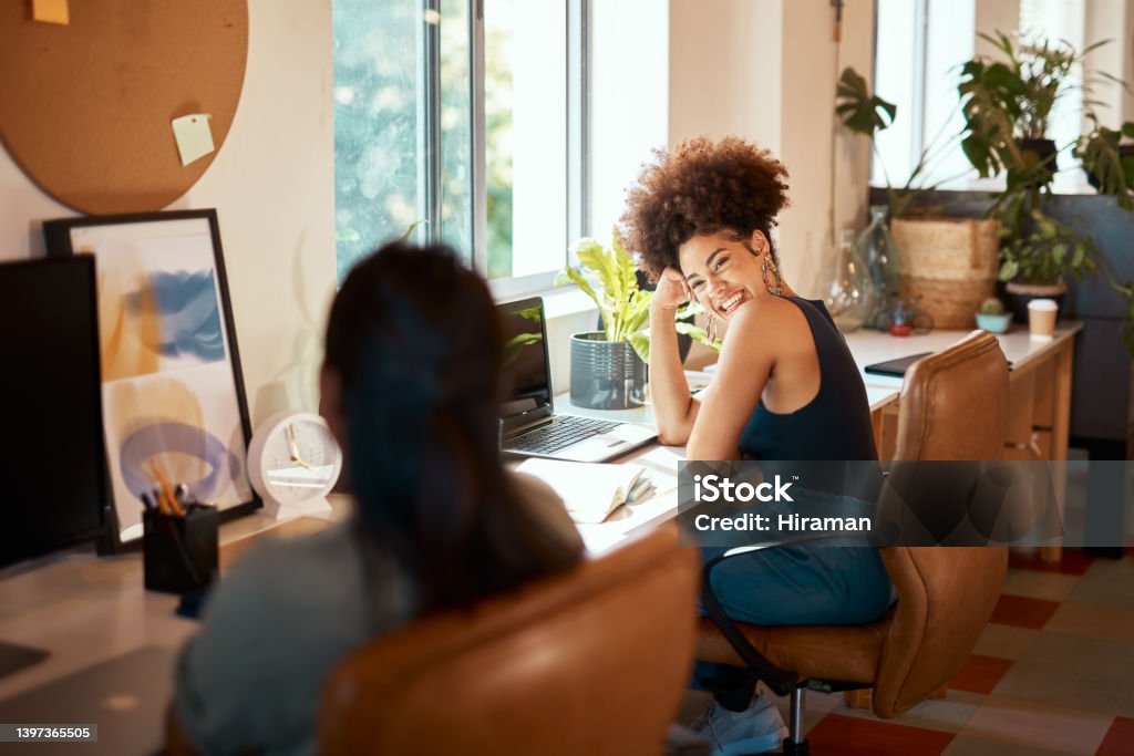 Beautiful mixed race creative business woman laughing with a female colleague. Two young female african american designers working in their office. Happy entrepreneurs make the most productive workers Working Stock Photo