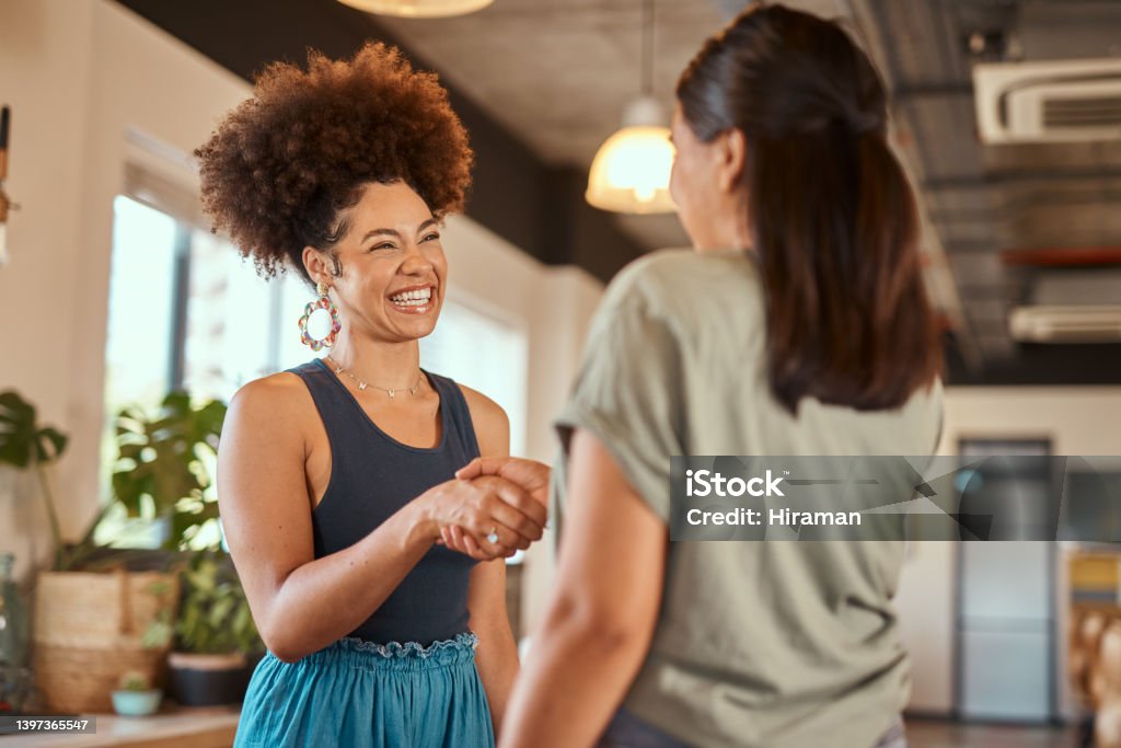 Beautiful mixed race creative business woman shaking hands with a female colleague. Two young female african american designers making a deal. A handshake to congratulate a coworker on their promotion Handshake Stock Photo