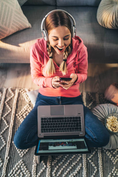 Young woman using her smartphone and laptop at home stock photo