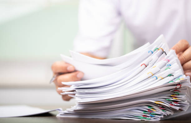 Man in a white shirt sign contract agreement documents in Stack of Group report papers clipped in color clips in fair light, business.