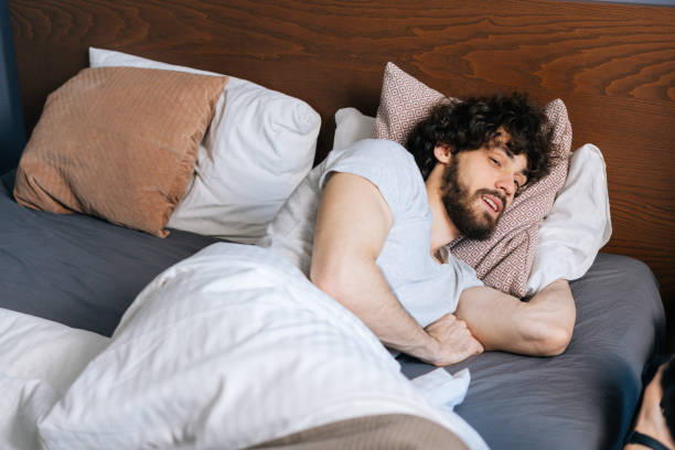 istock High-angle view of bearded young man sleeping with open eyes peacefully lying on back in large comfortable double bed under white blanket 1397371429