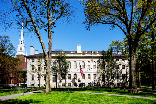 Cambridge, Massachusetts, USA - May 13, 2022:  View across Harvard Yard of the white University Hall building (c. 1813) with the John Harvard monument (c. 1884) in front of it. The Memorial Church is to the left in the background.