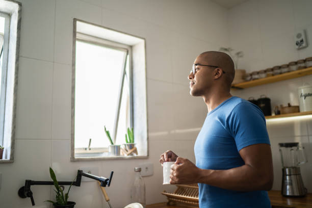 Contemplative young man drinking coffee or tea and looking window at home