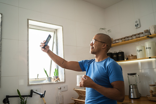 Young man filming or taking a selfie using mobile phone at home