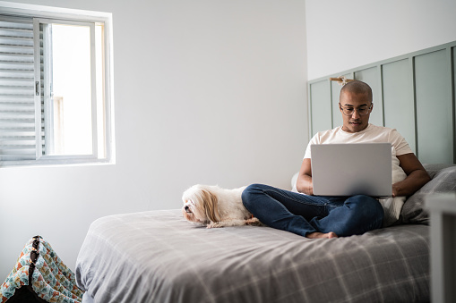 Young man using the laptop with the dog in the bed at home