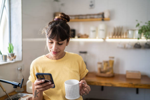 집에서 커피나 차를 마시면서 휴대폰을 사용하는 젊은 여성 - telegram 뉴스 사진 이미지
