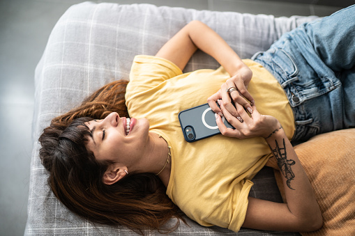 Young woman lying down in the bed holding the mobile phone at home