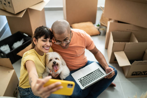 Young couple taking a selfie or filming using mobile phone while packing moving boxes at home