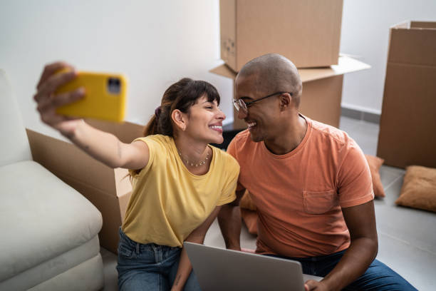 istock Young couple taking a selfie or filming using mobile phone while packing moving boxes at home 1397373504