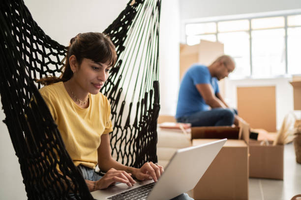 istock Young woman using laptop and her husband packing and moving boxes at new home 1397373621