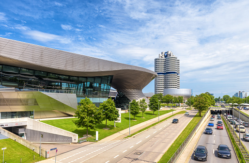 Munich - Aug 2, 2019: BMW Welt building and car road in Munich, Bavaria, Germany. World headquarters tower or BMW four-cylinder in distance. Munchen cityscape with landmarks and traffic in summer.