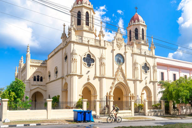 Havana, Cuba - May 24, 2022: A person rides a bicycle in front of the Catholic church named 'Parroquia Santa Catalina de Siena'. The religious building is located in the intersection of Paseo y Calle 25 in El Vedado district