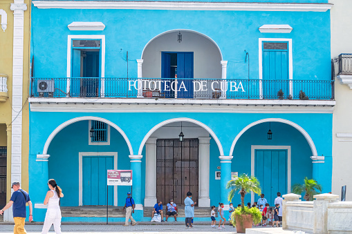 Havana, Cuba - May 24, 2022: A group of people are seen in their daily life by the Fototeca de Cuba. The colonial building is located in the Plaza Vieja in Old Havana.