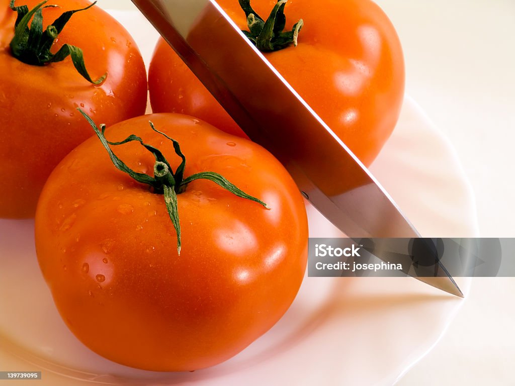 Tomatos and knife Three tomatos and knife on the plate. Cooking Stock Photo