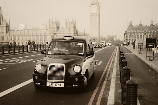 Old looking black cab taxi with a vintage retro sepia photo filter on Westminster Bridge in London