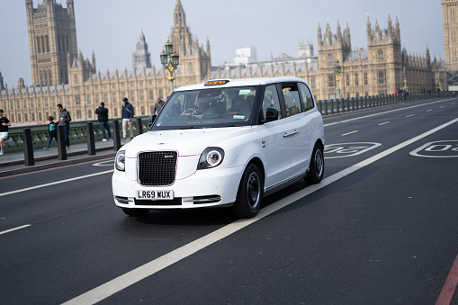White electric taxi on Westminster Bridge in London with Big Ben and Westminster Palace in the background