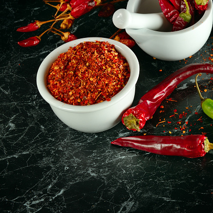 A selection of dried spices and herbs spilling out from glass jars onto a dark slate background. \nCoriander seed, cloves, cardamom, cinnamon sticks, chilli powder, turmeric and fresh bay leaves. \nLow angle view with copy space to the right of the image.  \nClose up.