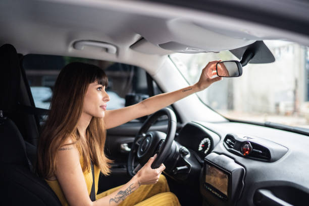 young woman arranging rearview mirror in the car - car test drive car rental women imagens e fotografias de stock