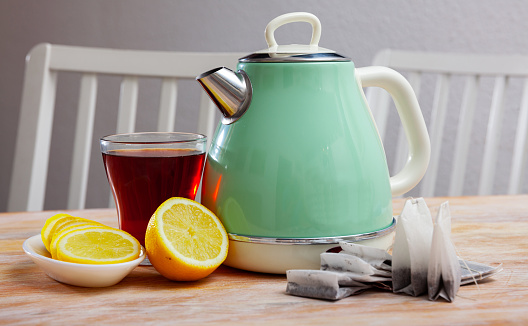 Teatime. Retro style turquoise electric kettle, cup of tea and sliced lemon on wooden kitchen table