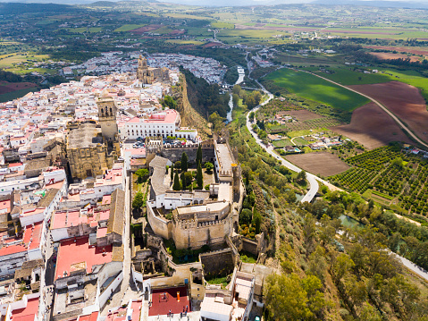 Aerial view of medieval fortified Castle in Andalusian town of Arcos de la Frontera atop sandstone ridge on bank of Guadalete river, Spain