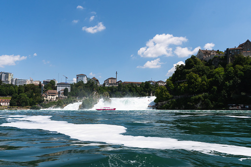 A boat with tourist drives along the Rhine Falls in Switzerland which are one of the largest waterfalls in Europe.