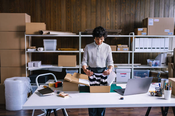 A Smart Businesswoman Preparing Packages For Shipping  In Her Store A beautiful female Latin-American entrepreneur packing clothes for delivery  in cardboard boxes. market vendor stock pictures, royalty-free photos & images