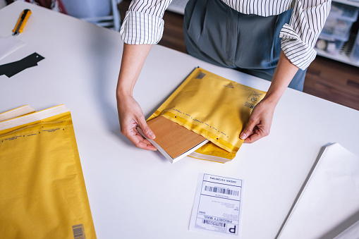 A from above view of an anonymous Caucasian entrepreneur packing a book in a yellow envelope for delivery.