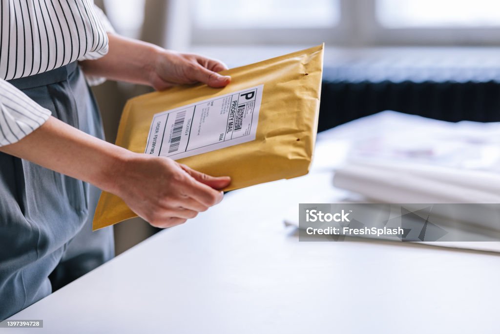 An Unrecognizable Businesswoman Preparing A Package For Shipping An anonymous Caucasian entrepreneur holding a yellow envelope with a label on it, making it ready for delivery. Envelope Stock Photo