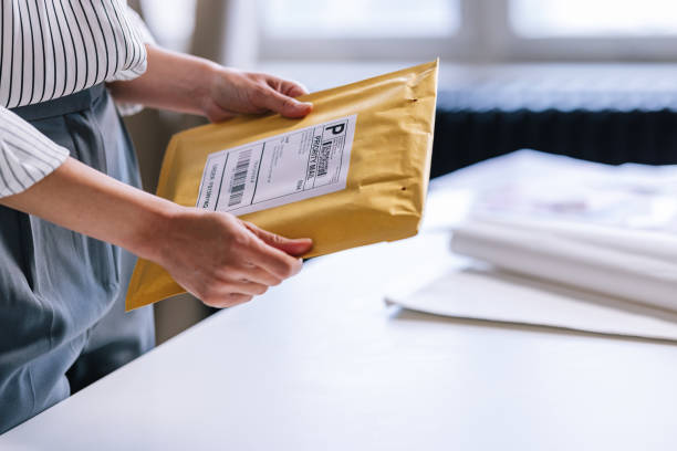 An Unrecognizable Businesswoman Preparing A Package For Shipping An anonymous Caucasian entrepreneur holding a yellow envelope with a label on it, making it ready for delivery. mail stock pictures, royalty-free photos & images