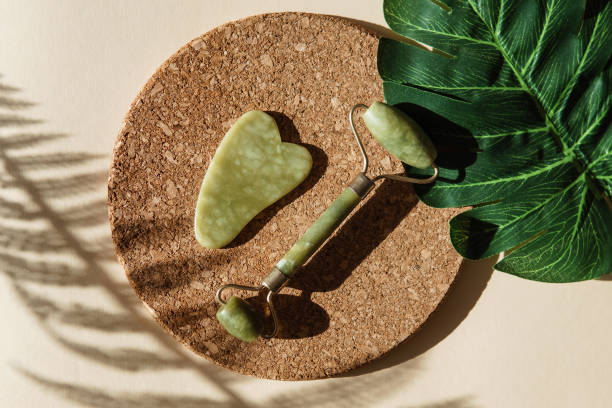 istock Jade Gua sha scraper and face roller massager on a cork round stand with a monstera leaf. 1397403191