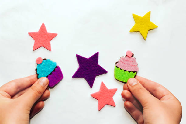 mãos de crianças fazem um aplique de adesivos de feltro de estrelas e cupcakes - appliqué - fotografias e filmes do acervo