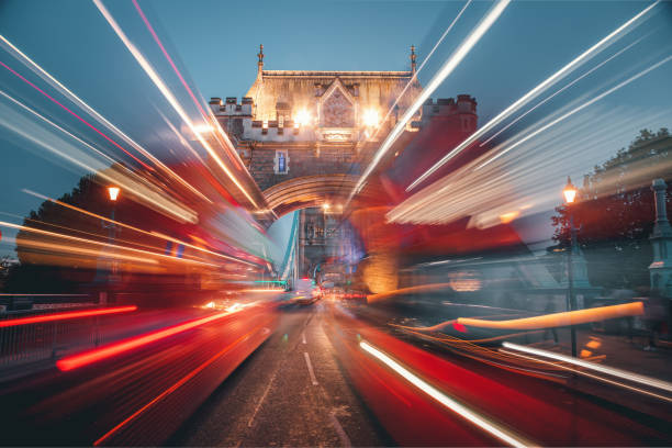 Blurred motion long exposure shot of two speeded double decker red buses at rush hour traffic at night on Tower Bridge in London, United Kingdom
