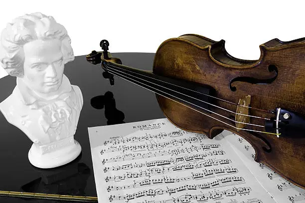 A violin, score, and bust of Beethoven atop a piano, isolated against a white background.