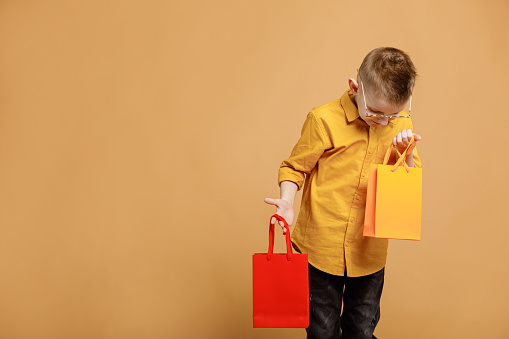 Shopping on black friday. Little boy holding shopping bags on yellow background. Shopper with many colored paper bags. Holidays sales and discounts. Cyber monday. High quality photo.