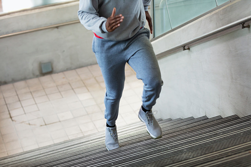 Cropped view of an African-American man in his 30s wearing a sweatshirt and sweatpants, running up the steep concrete staircase of a municipal building.